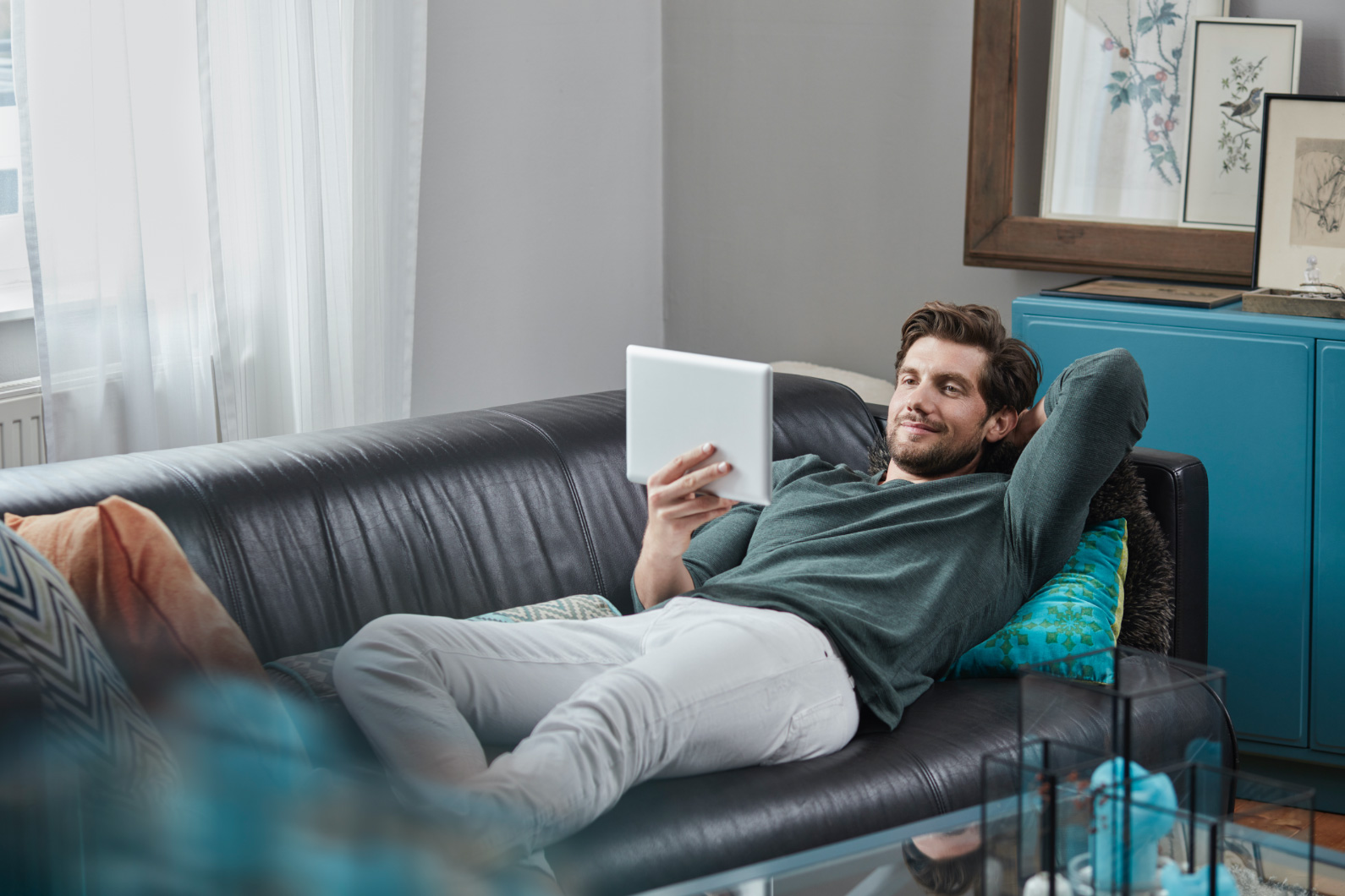 Foto de un hombre leyendo su tablet echado en el sofá