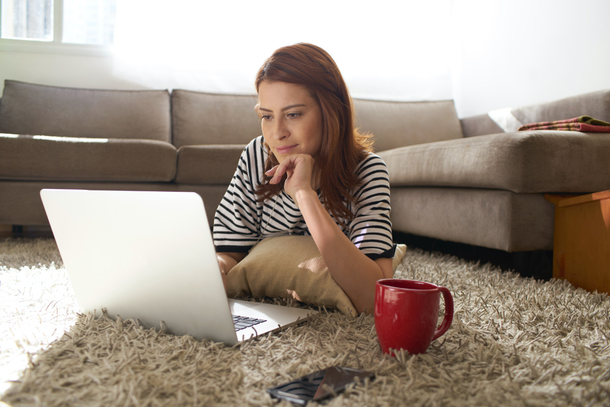 Foto de mujer mirando con interés su laptop con una taza de café al costado.